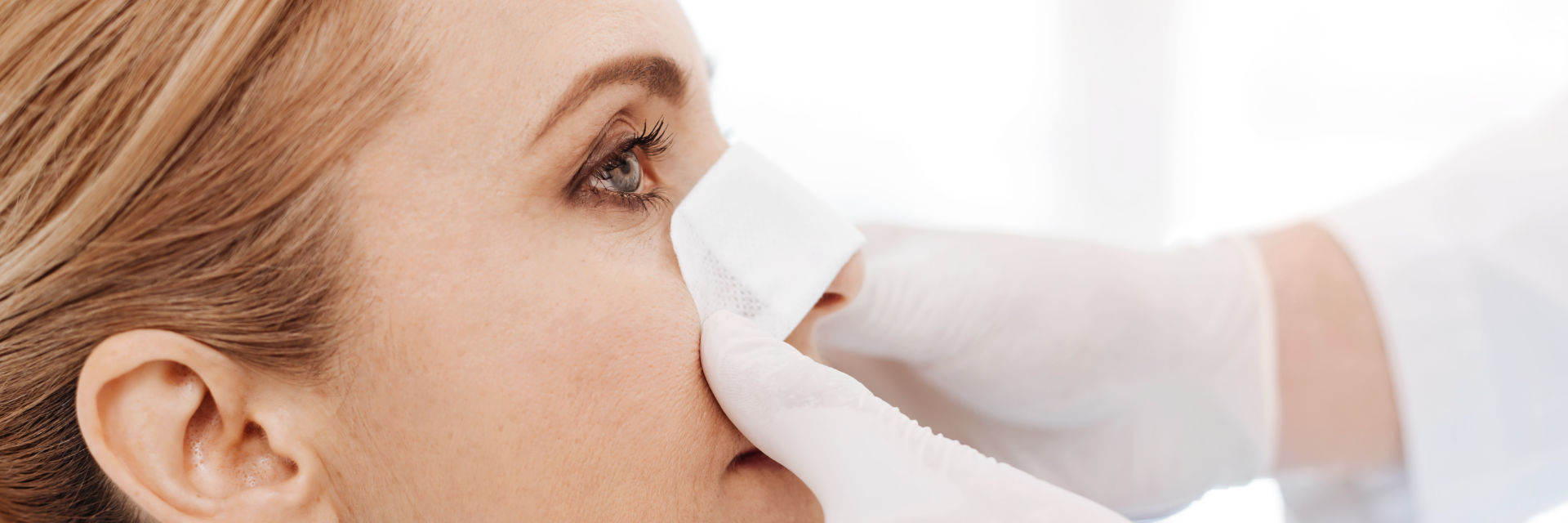 A doctor applying protective dressing on nose of a woman after nose procedure.