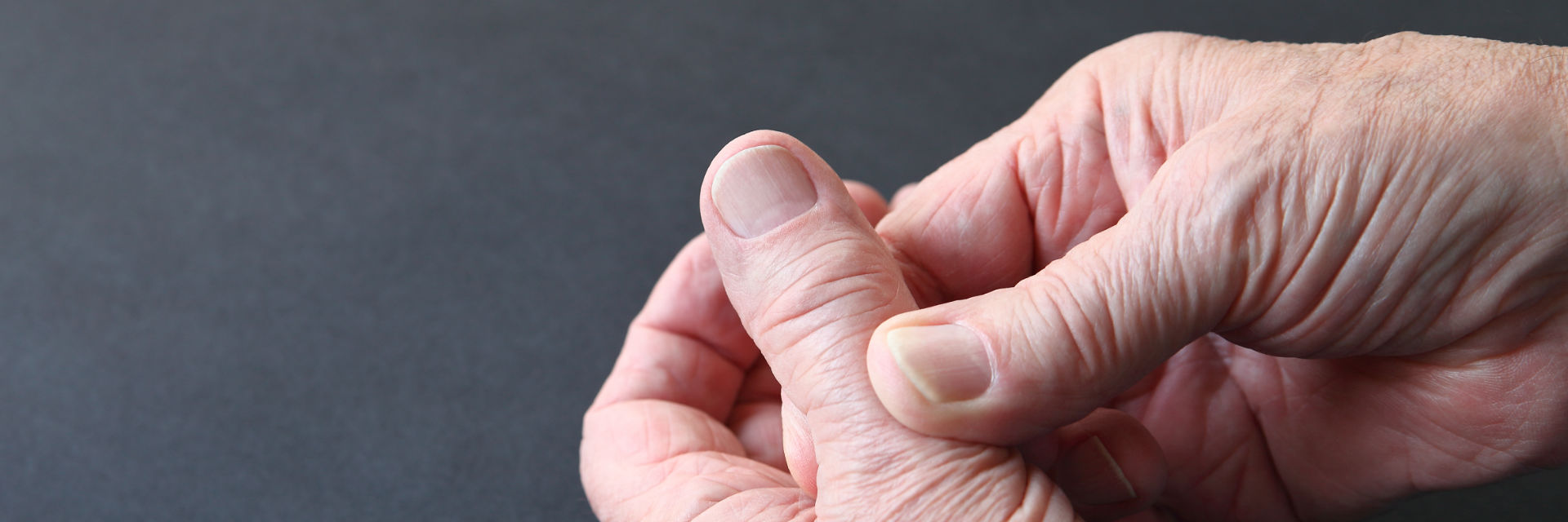 Elderly person touching their thumb due to pain.
