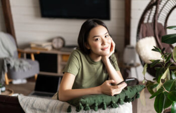 Haircare and beauty concept. Close up of happy smiling woman touches her natural hair, healthy glowing hair, white teeth and clean facial skin, standing against pink background.